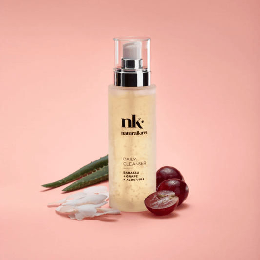 NK Daily Cleanser bottle with babassu, grape, and aloe vera on pink background, organic skincare product for daily use.