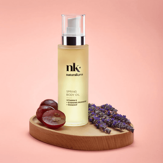 NK Spring Body Oil in a bottle with grapes and lavender on a wooden platter, promoting organic skincare.